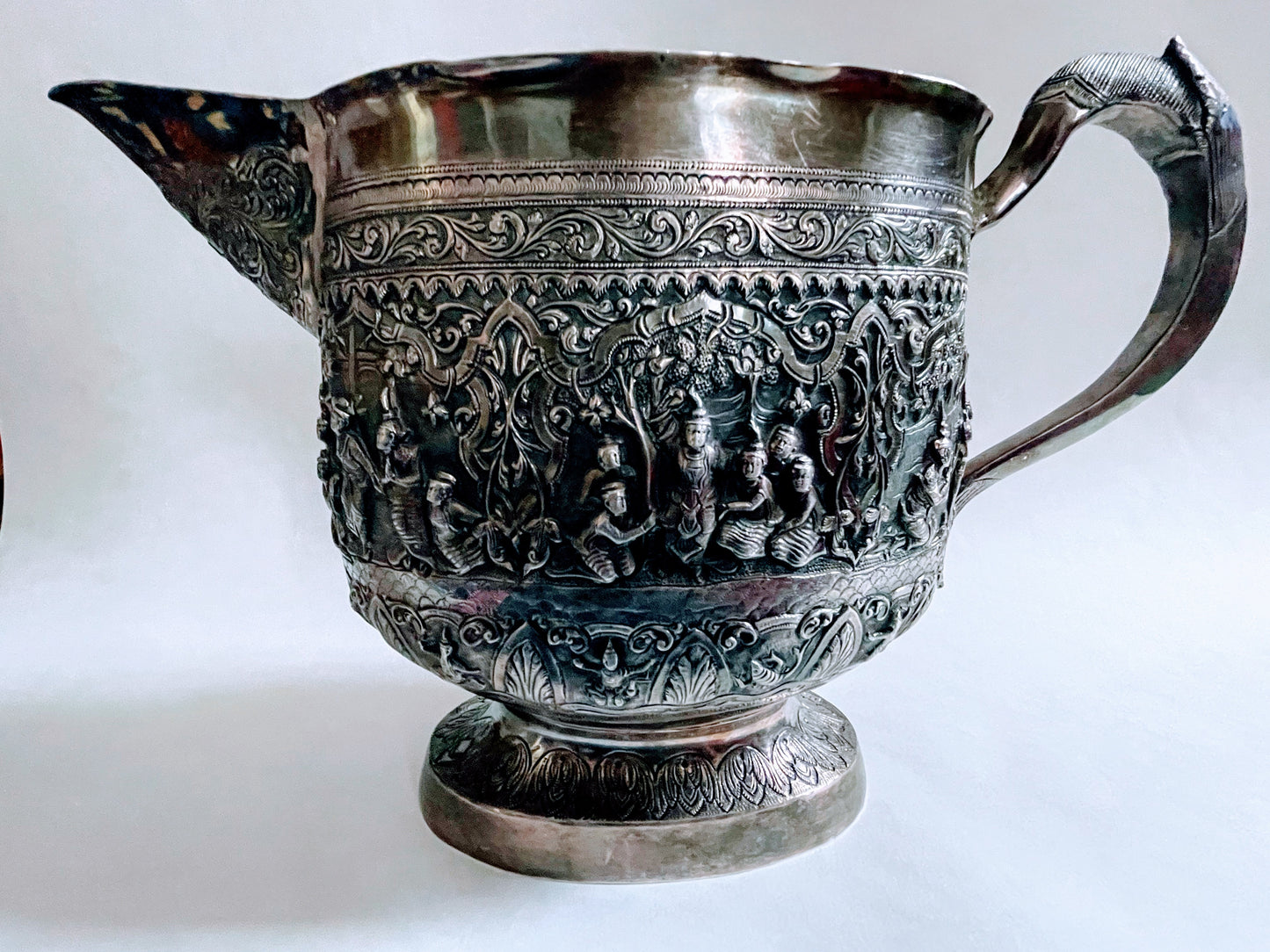 A Burmese antique elaborately carved circular tray and oval shaped jug with a pointed mug.