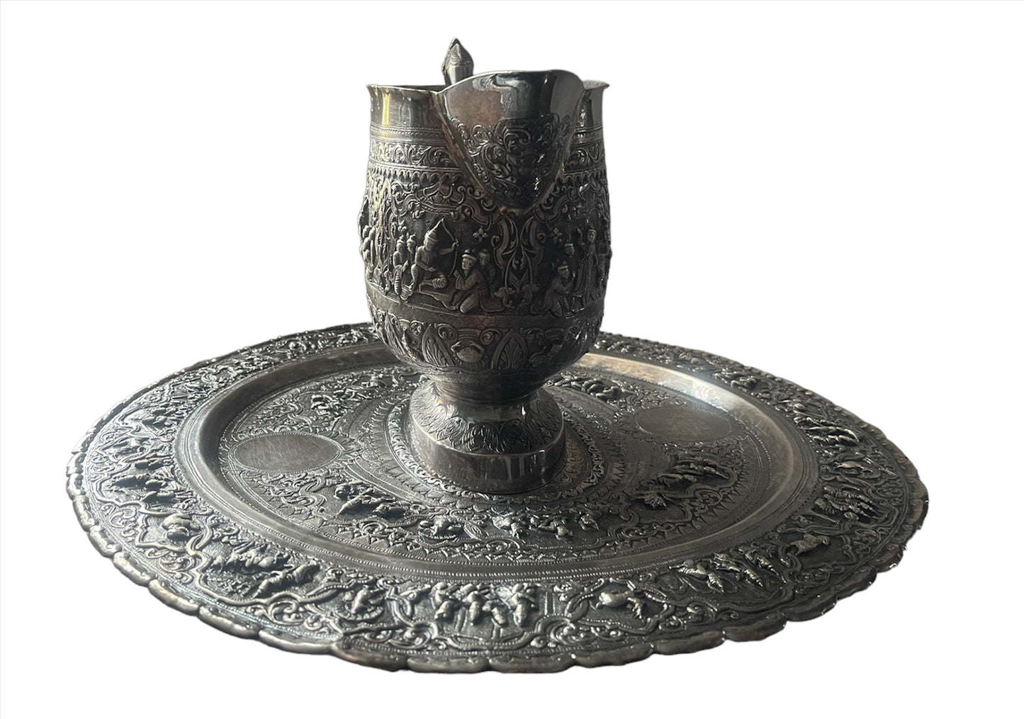 A Burmese antique elaborately carved circular tray and oval shaped jug with a pointed mug.