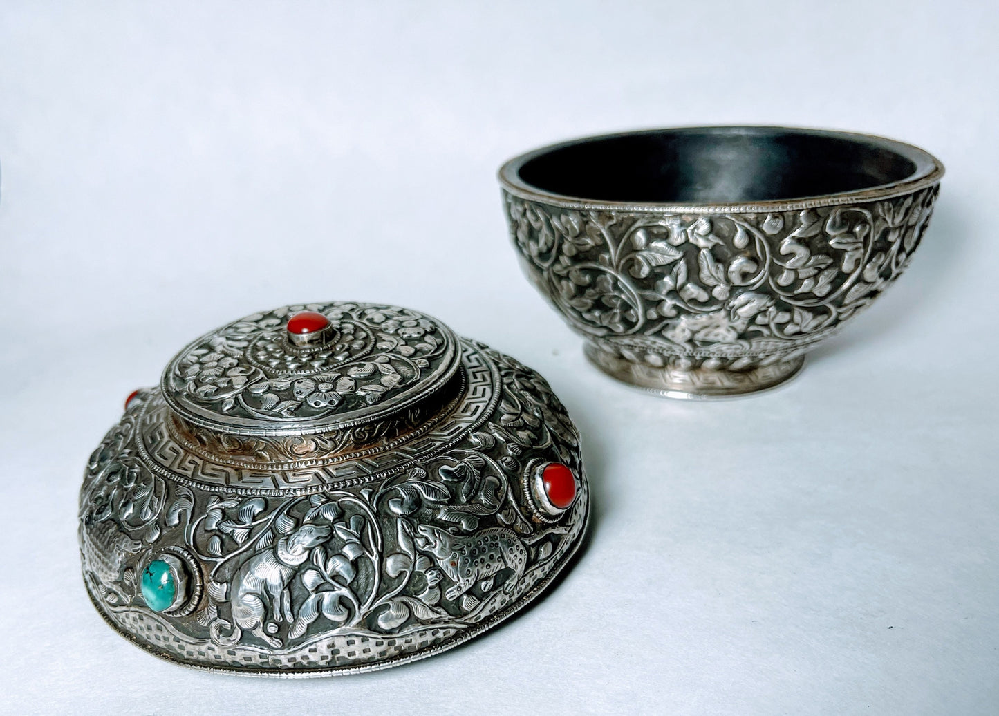 A vintage Tibetan silver covered wooden bowl with heavy carvings and turquoise and coral cabochons