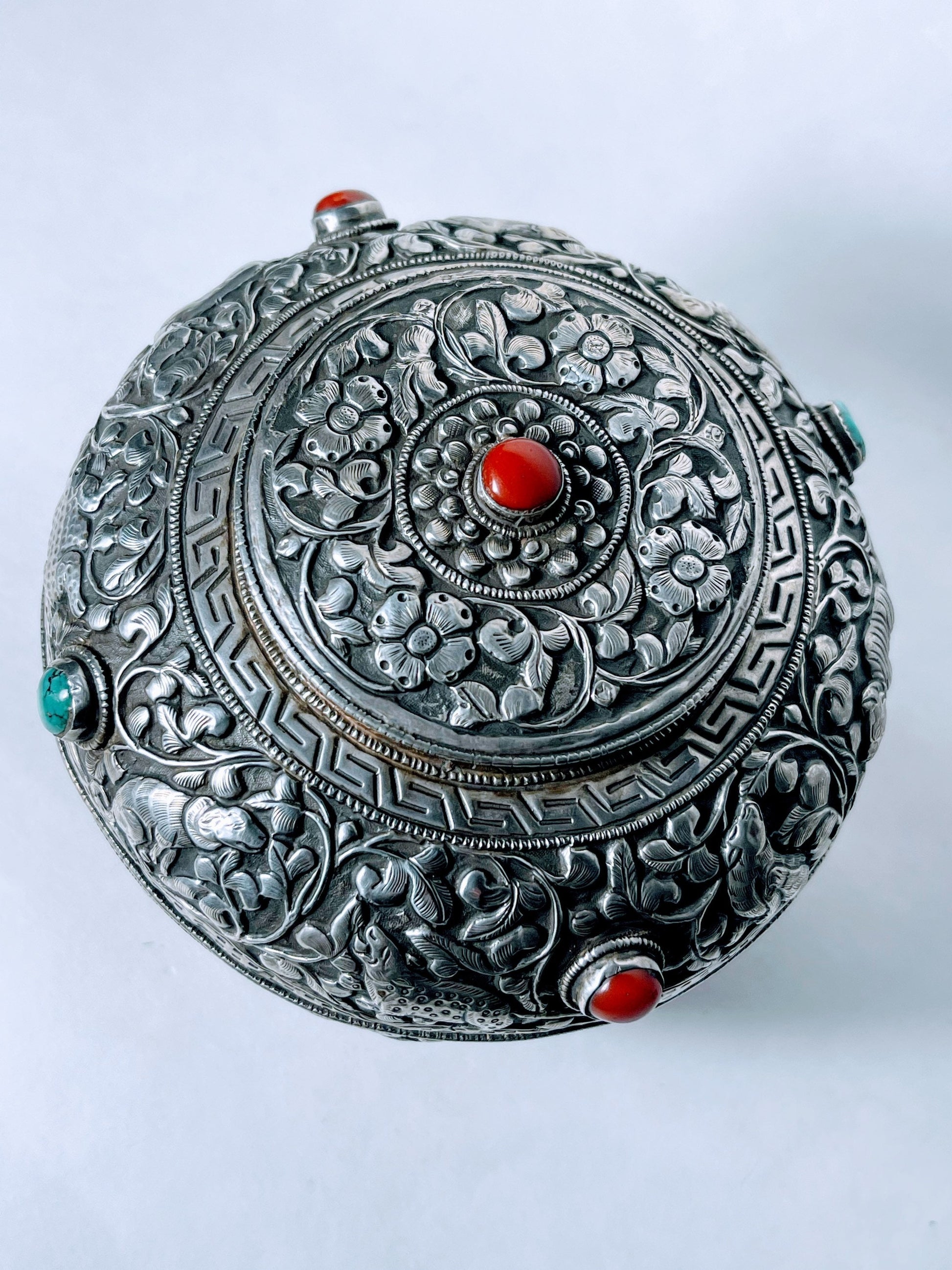 A vintage Tibetan silver covered wooden bowl with heavy carvings and turquoise and coral cabochons