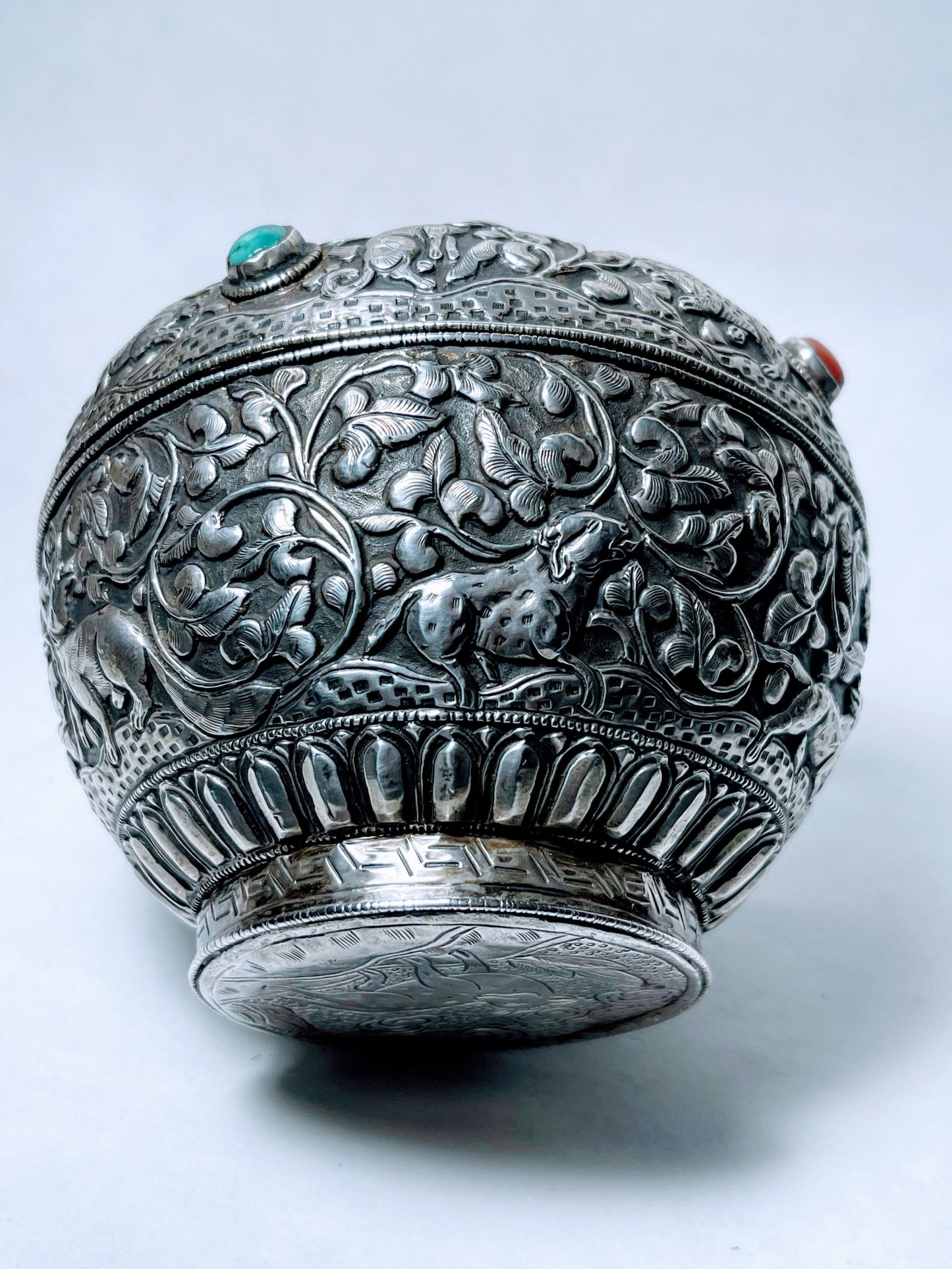 A vintage Tibetan silver covered wooden bowl with heavy carvings and turquoise and coral cabochons