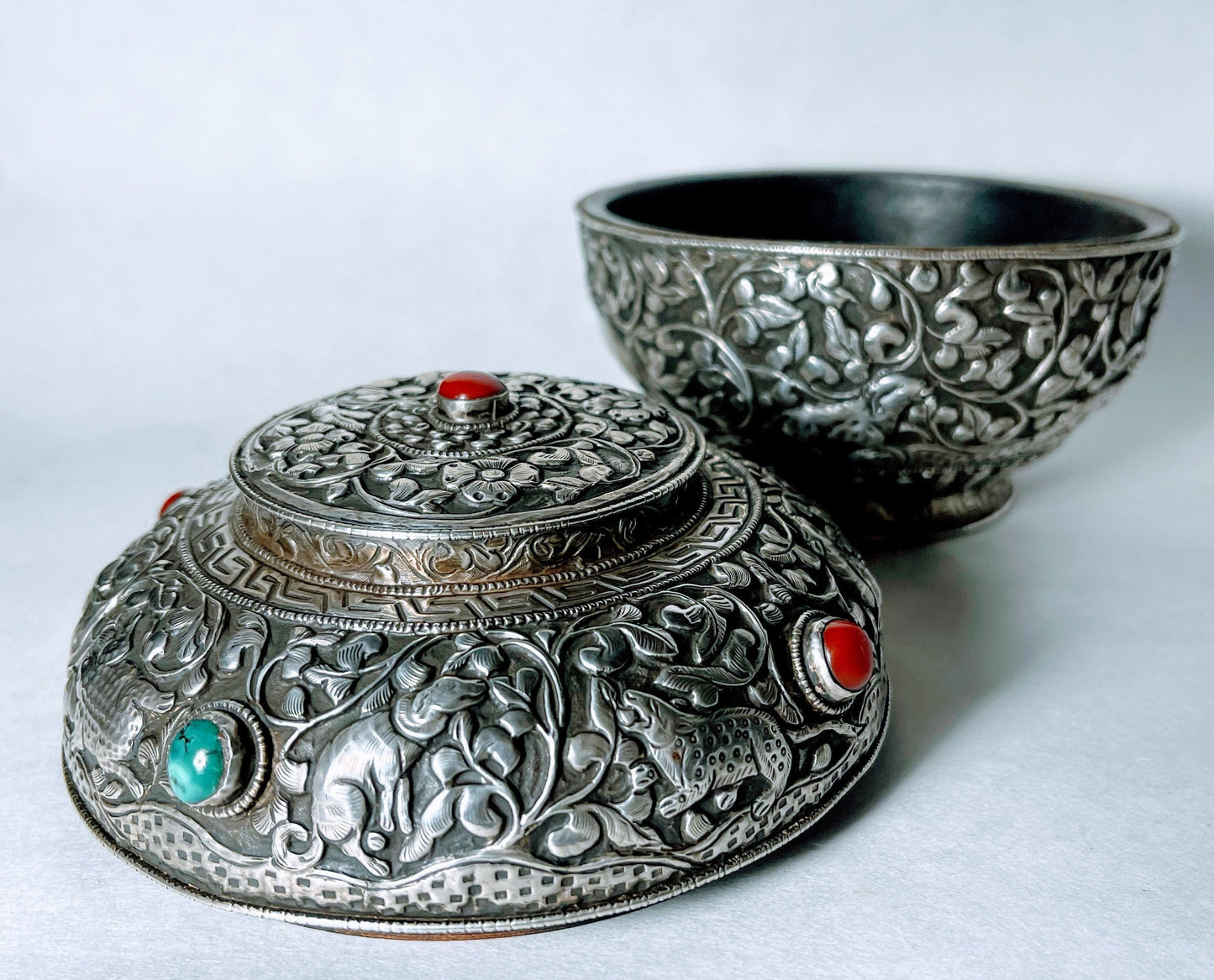 A vintage Tibetan silver covered wooden bowl with heavy carvings and turquoise and coral cabochons